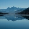 Snow-capped mountains reflected in a calm alpine lake Mountain lake reflecting snow-capped peaks under blue sky