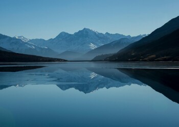 Snow-capped mountains reflected in a calm alpine lake Mountain lake reflecting snow-capped peaks under blue sky