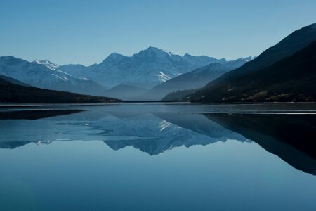 Snow-capped mountains reflected in a calm alpine lake Mountain lake reflecting snow-capped peaks under blue sky