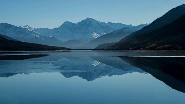 Snow-capped mountains reflected in a calm alpine lake Mountain lake reflecting snow-capped peaks under blue sky