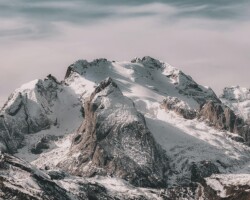 Snow-covered mountain range under cloudy sky Snowy mountain peaks with cloudy sky
