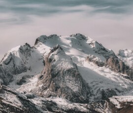 Snow-covered mountain range under cloudy sky Snowy mountain peaks with cloudy sky